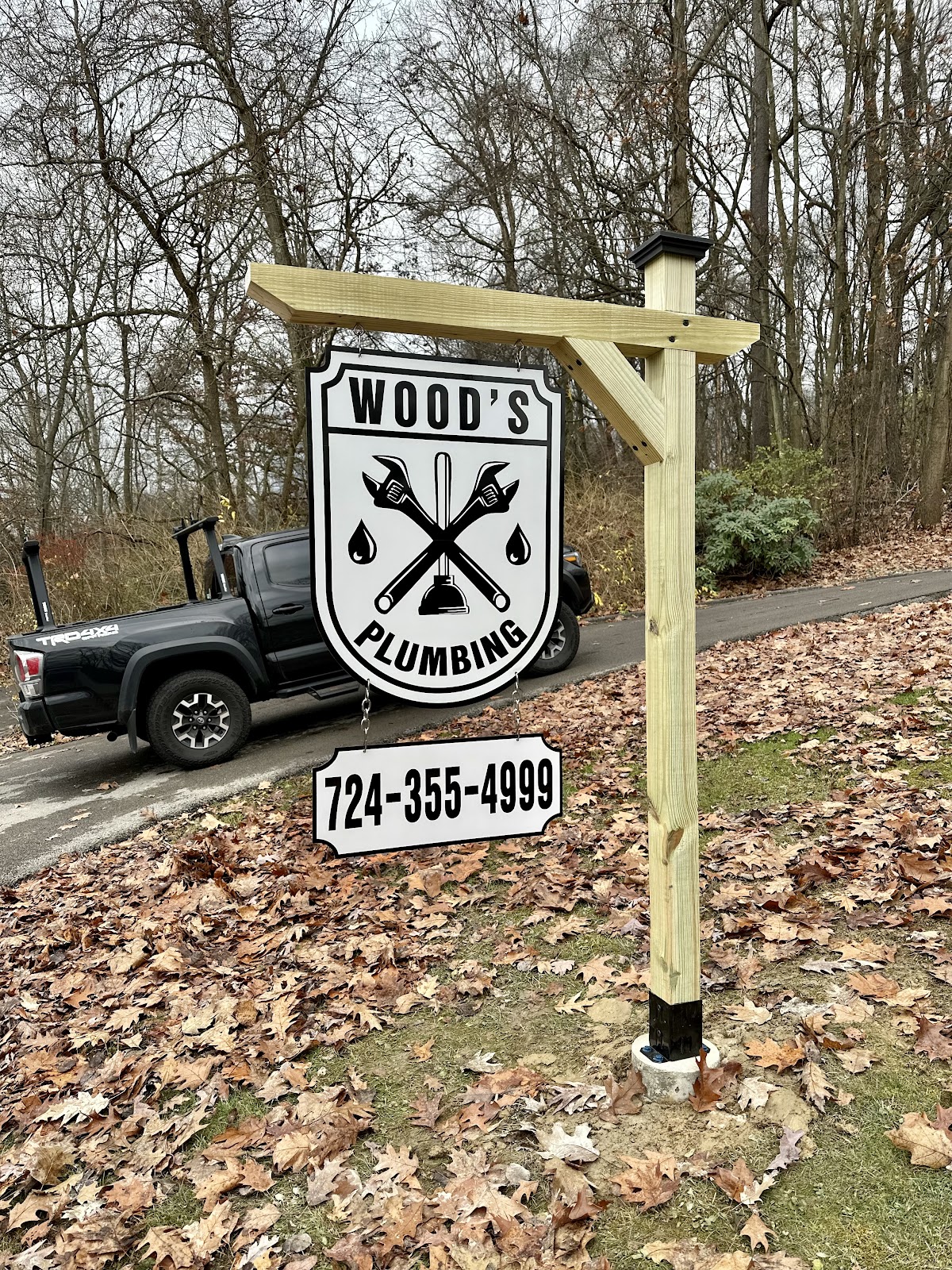 Wood's Plumbing hand-built roadside sign with the company crest and phone number, next to Ben's work truck