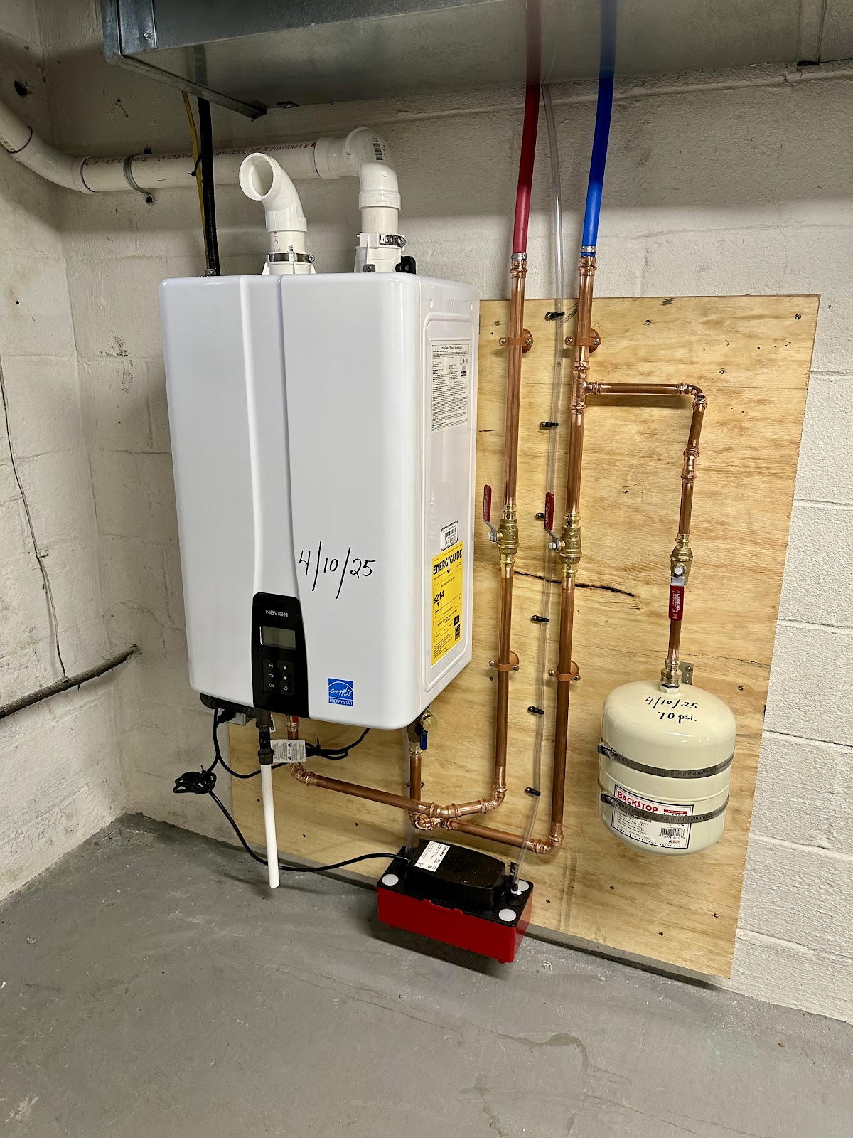 New tankless Navien water heater installed with color-coded copper supply lines and an expansion tank
