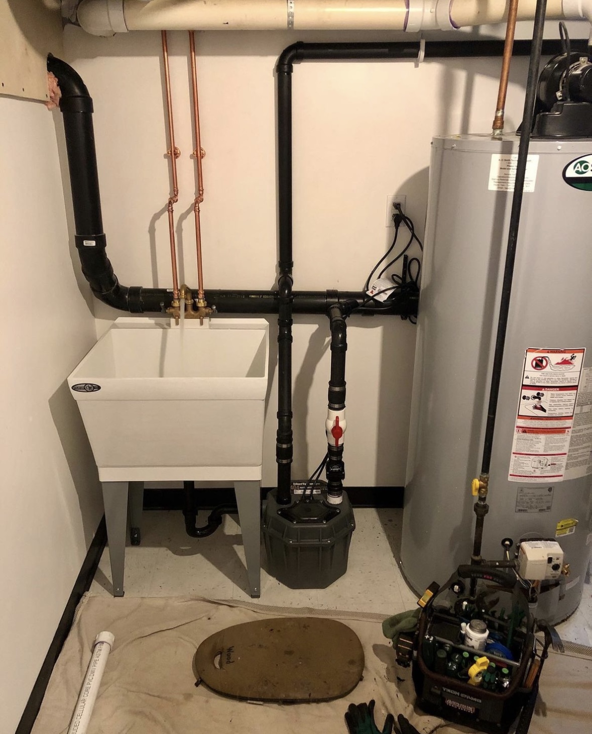 Completed utility sink, water heater, and sump pump installation with neat copper and labeled ABS pipe